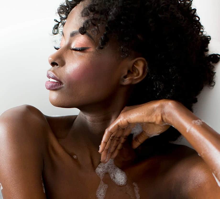 Woman sitting in a bath with bubbles on her arm