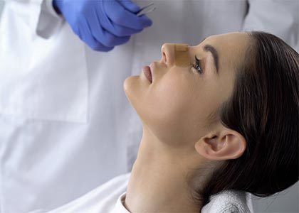 Lady with plaster on nose, doctor examining patients face after plastic surgery