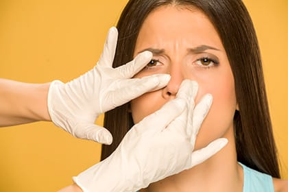 Doctor's hands checking the nose of a young woman on yellow background