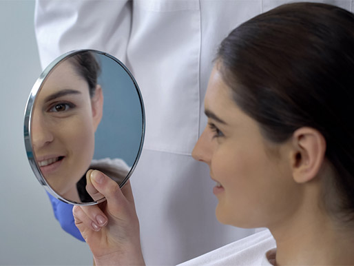 Young female satisfied with rhinoplasty result, smiling face reflected in mirror