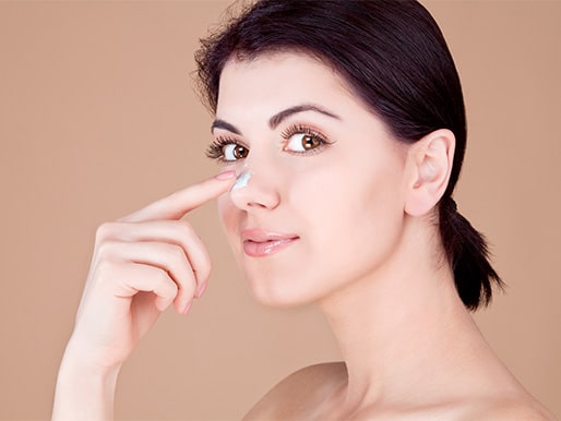 Girl touching her nose with cream on a beige background.