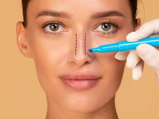 Plastic surgeon drawing pre-surgical lines on woman's nose.