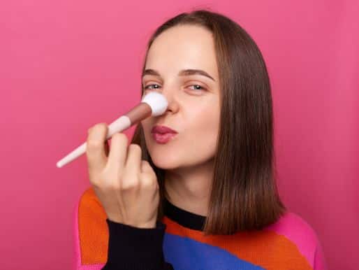 A beautiful young woman putting make-up on her nose to make it look better.