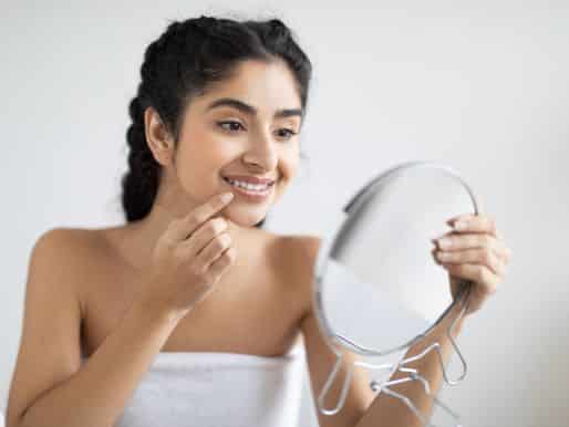 Smiling woman touching her lips and looking at her face in the mirror